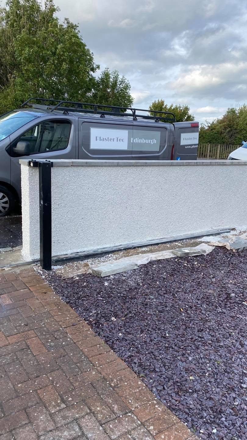 Freshly plastered white wall with a service van parked behind it on a gravel driveway.