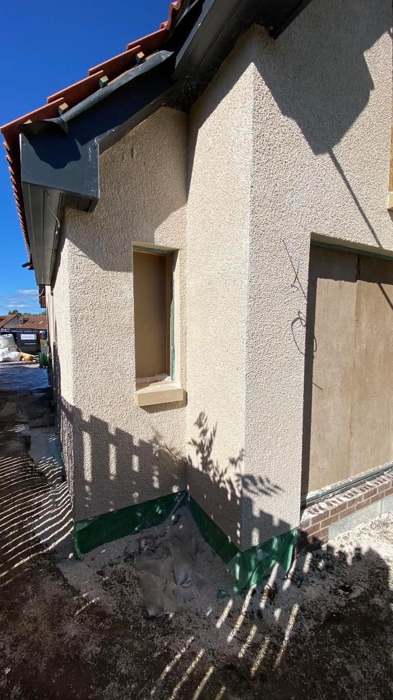 Textured beige exterior wall featuring a narrow window opening and a larger boarded-up doorway.