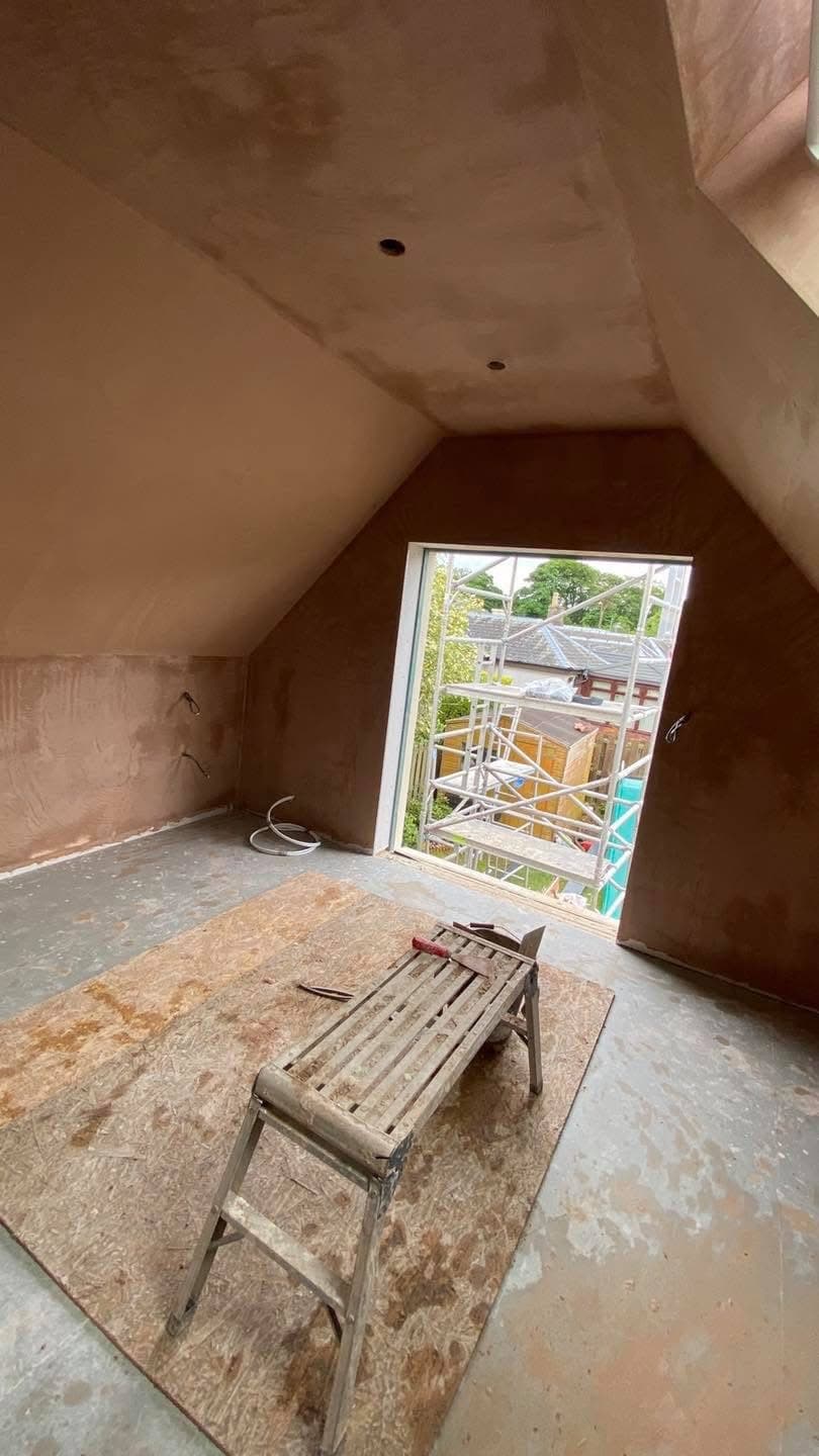 Freshly plastered attic room with sloped ceilings, a metal step platform, and scaffolding outside.