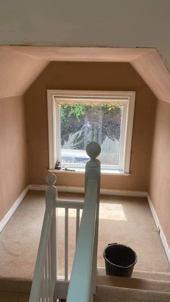 Freshly plastered landing area with a white window, sloped ceiling, and white staircase banister.
