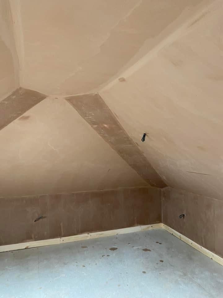 Freshly plastered attic room with sloped ceilings, wooden baseboards, and exposed electrical wiring.
