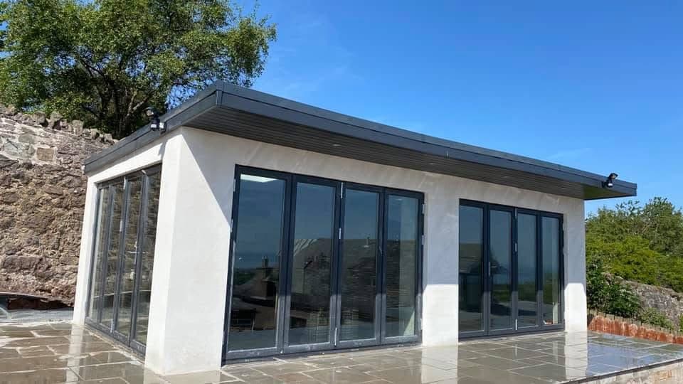 Modern white garden studio featuring large dark grey bi-fold glass doors and flat roof.